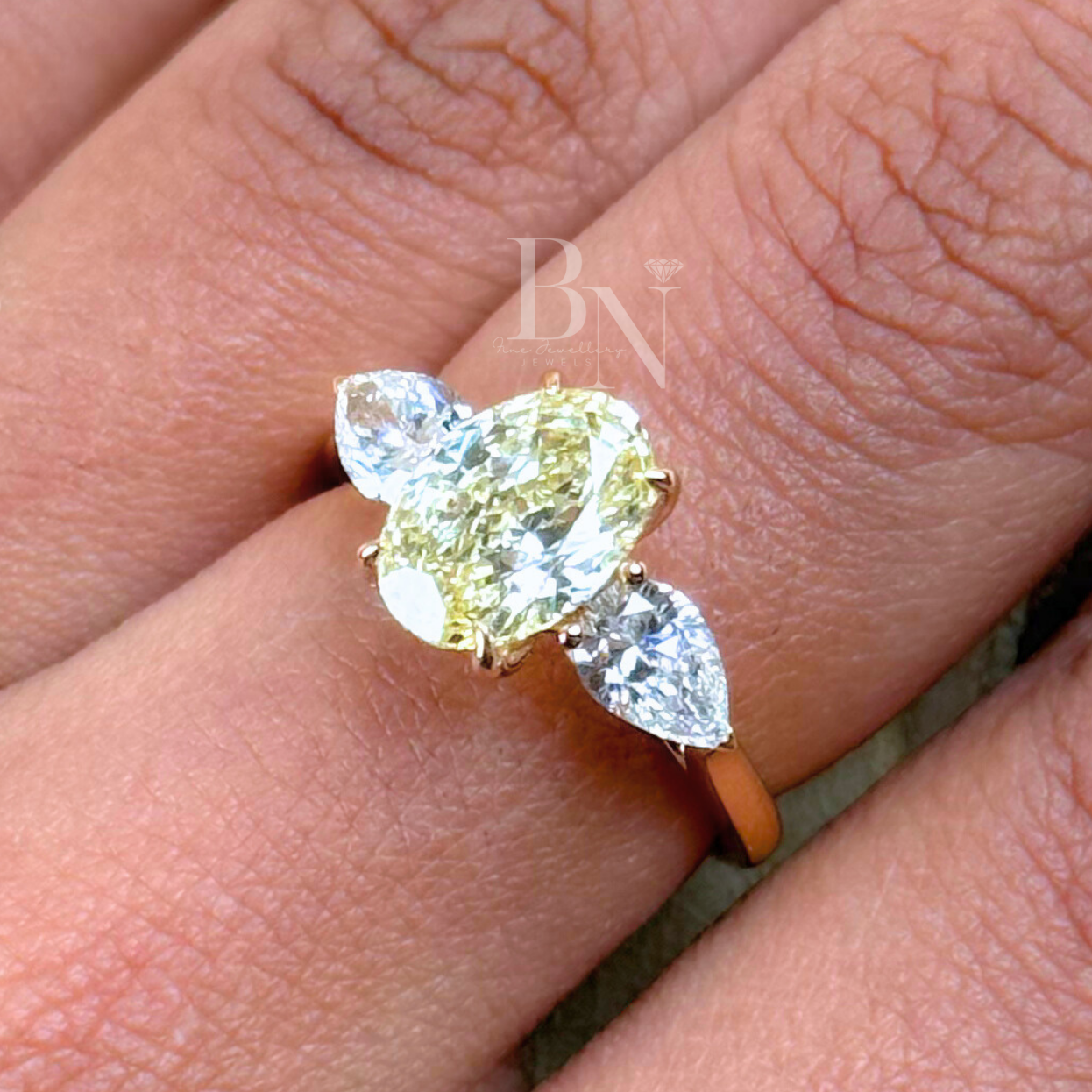Top view of a 1.80 carat fancy yellow oval lab grown diamond engagement ring with two brilliant pear-shaped side stones in a solid yellow gold setting, showing exceptional white light return and a three-stone trilogy design.