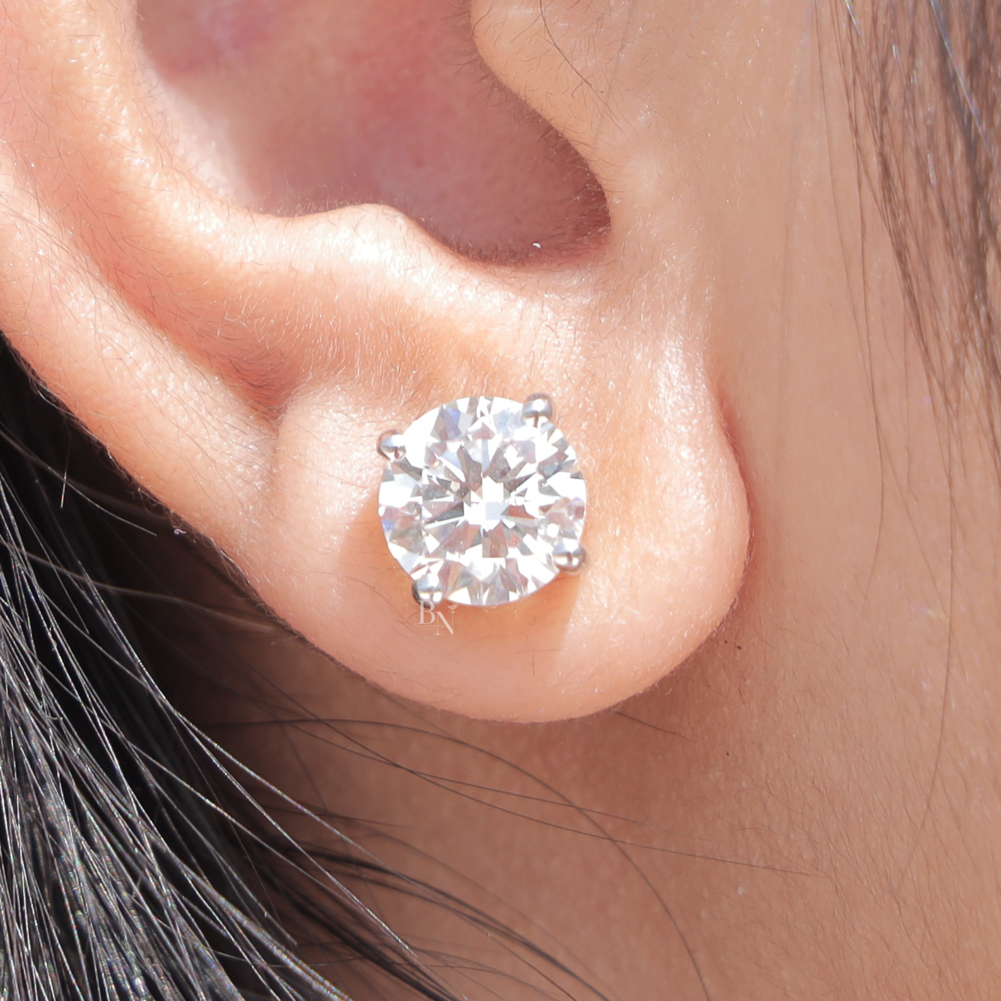 Close up of 4 carat total weight round brilliant cut lab grown diamond stud earrings in a two tone 14k yellow gold basket setting with secure screw back closures showing exceptional clarity and white light brilliance on a model.