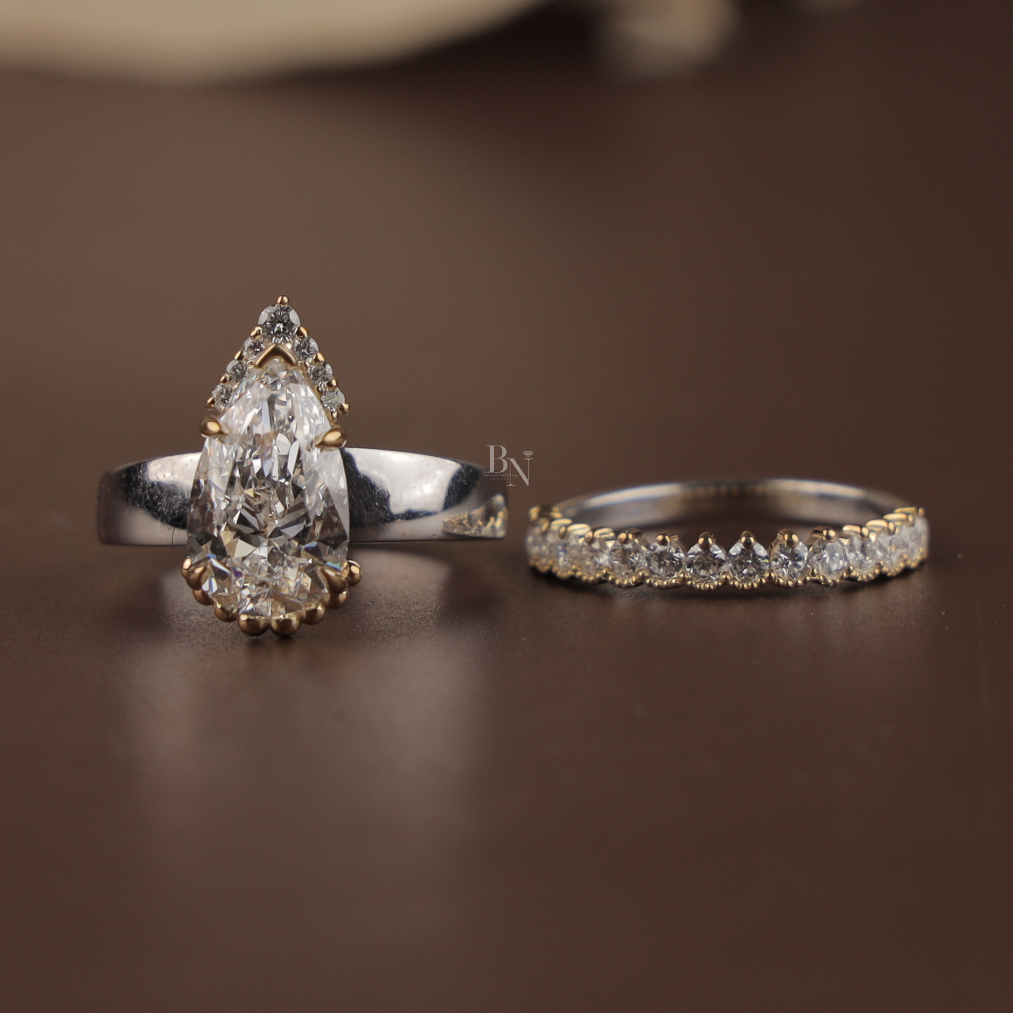 Close up of a 2.5 carat pear cut lab grown diamond engagement ring with a hidden halo setting and matching pave diamond wedding band in 14k white gold on a model's hand.