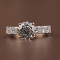 3 carat round brilliant cut lab grown diamond engagement ring with compass prongs and princess cut diamond accents on a 14k yellow gold band.