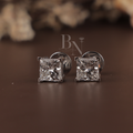 May include: Two square-cut diamond stud earrings set in silver metal, presented in a black jewellery box with a velvet lining. The diamonds are shown sparkling. The earrings are a classic design.