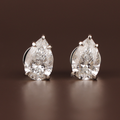 May include: A pair of pear-cut diamond stud earrings. Each earring showcases a clear, faceted diamond set in a silver-coloured metal. The diamonds are the focal point, reflecting light against a dark brown background.