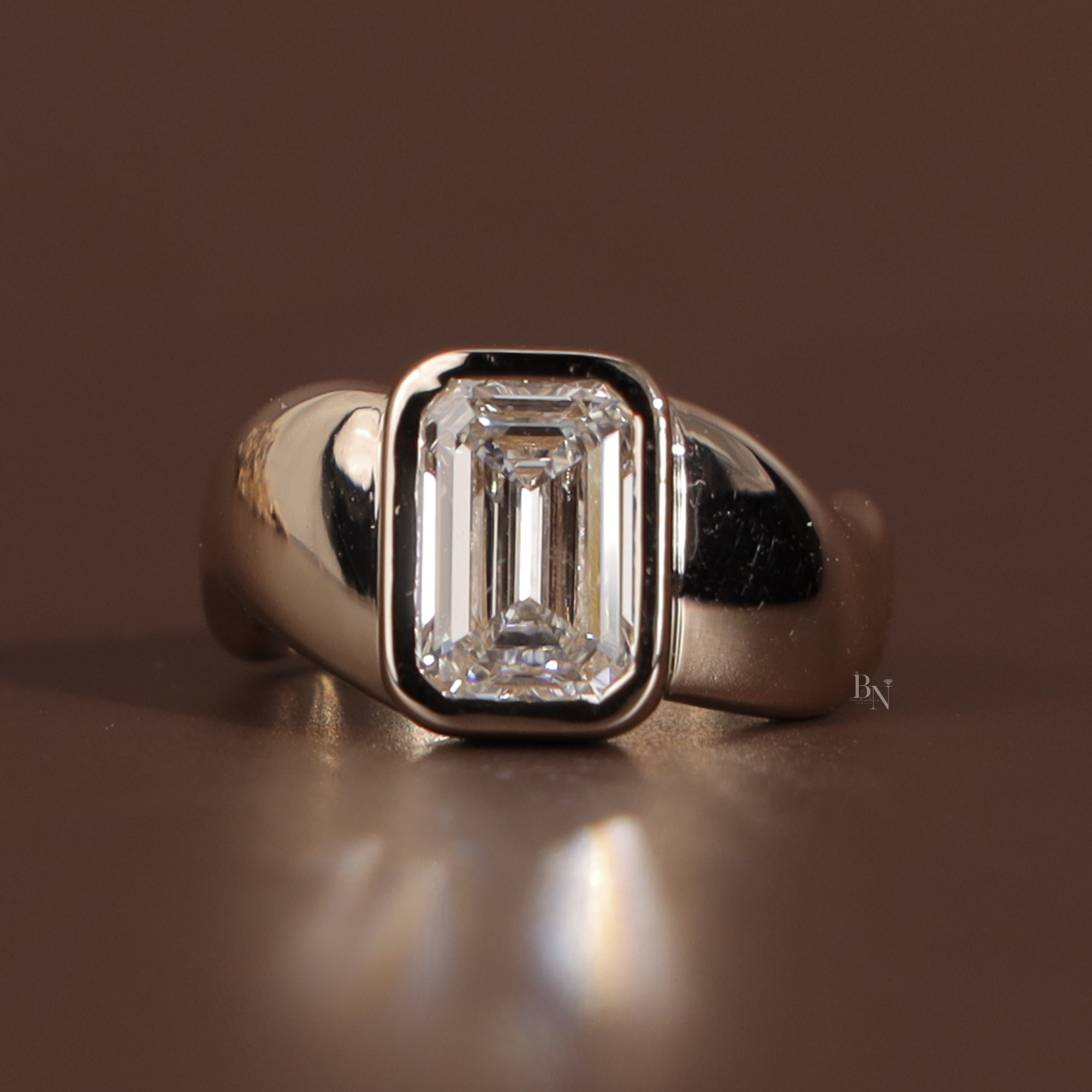 Front view of a 3 carat emerald cut lab grown diamond set in a secure 14k yellow gold full bezel setting with a bold, wide signet-style band, showcasing clean step-cut facets and a modern low-profile design.