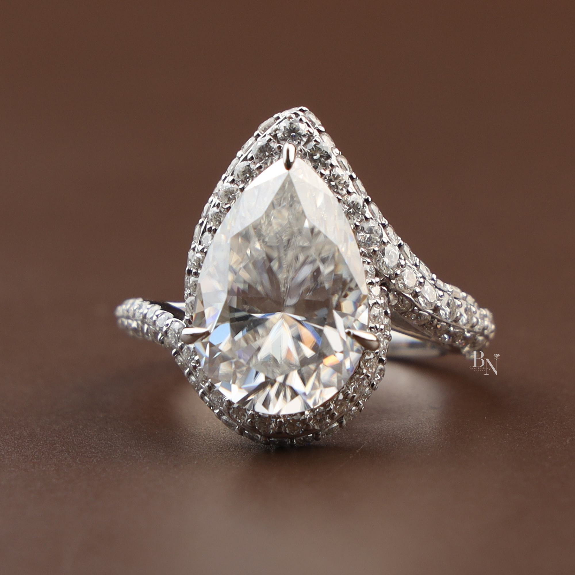 Stunning 5.50ct pear moissanite bypass ring in 14k white gold highlighting the intense rainbow fire and disco ball effect of the double tiered halo and shimmering triple-row pavé shank on a model's hand.