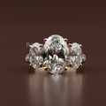 A 4 carat graduated three stone oval lab grown diamond engagement ring crafted in solid rose gold featuring sparkling pave diamond accents on the band shown from the front side profile and on a hand.