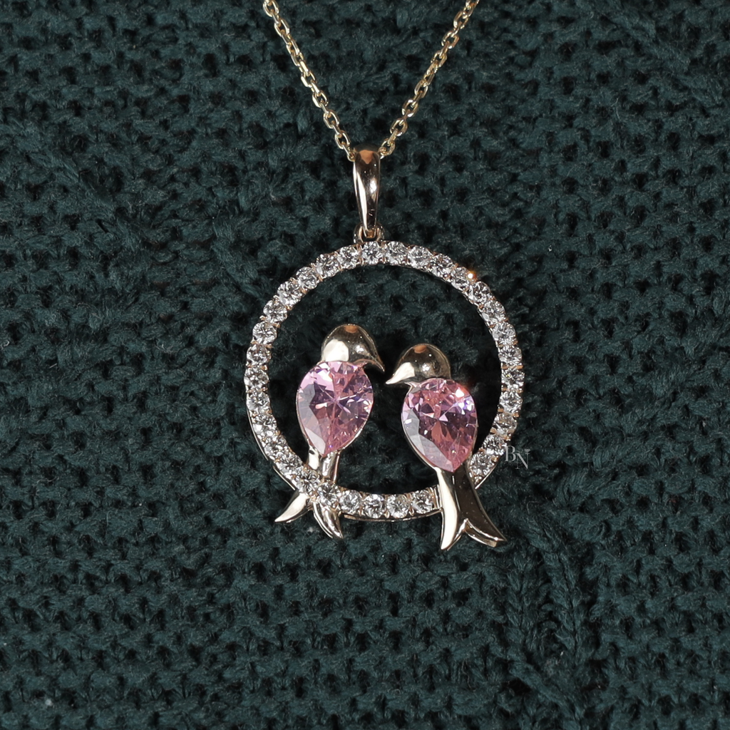 Macro shot of two pink pear cut lab grown diamonds shaped as birds inside a circular pavé diamond halo pendant in 14k white gold on a dainty chain.