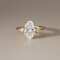 2.5 carat elongated oval lab grown diamond center stone flanked by two brilliant pear shaped side diamonds in a solid 14k yellow gold three stone setting with a polished cathedral band and secure gold prongs.