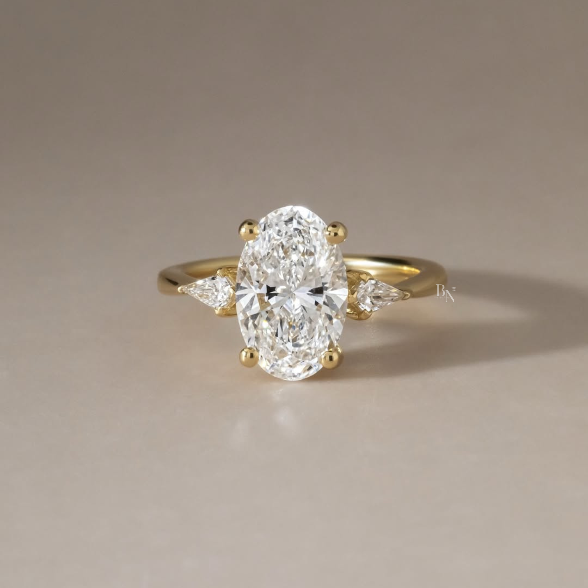 2.5 carat elongated oval lab grown diamond center stone flanked by two brilliant pear shaped side diamonds in a solid 14k yellow gold three stone setting with a polished cathedral band and secure gold prongs.