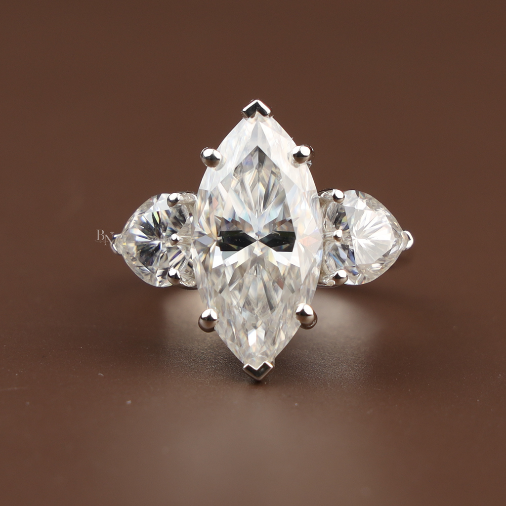 5.50 carat marquise cut lab grown diamond three stone engagement ring with heart shaped side diamonds in 14k white gold showing V-tip prongs and brilliant scintillation.