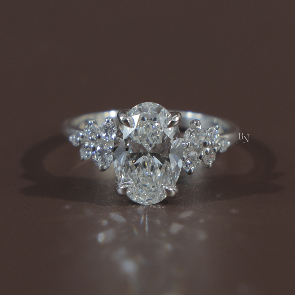 Hand view of 2 carat oval cut lab grown diamond engagement ring in 14k white gold featuring a brilliant center stone and unique floral cluster side diamonds on a thin polished band for a modern bridal look.