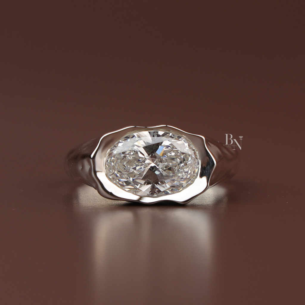 Three carat oval lab grown diamond engagement ring in a heavy platinum molten metal signet setting featuring an east west oriented fluid wavy bezel band design shown from the top profile and inside a black ring box.