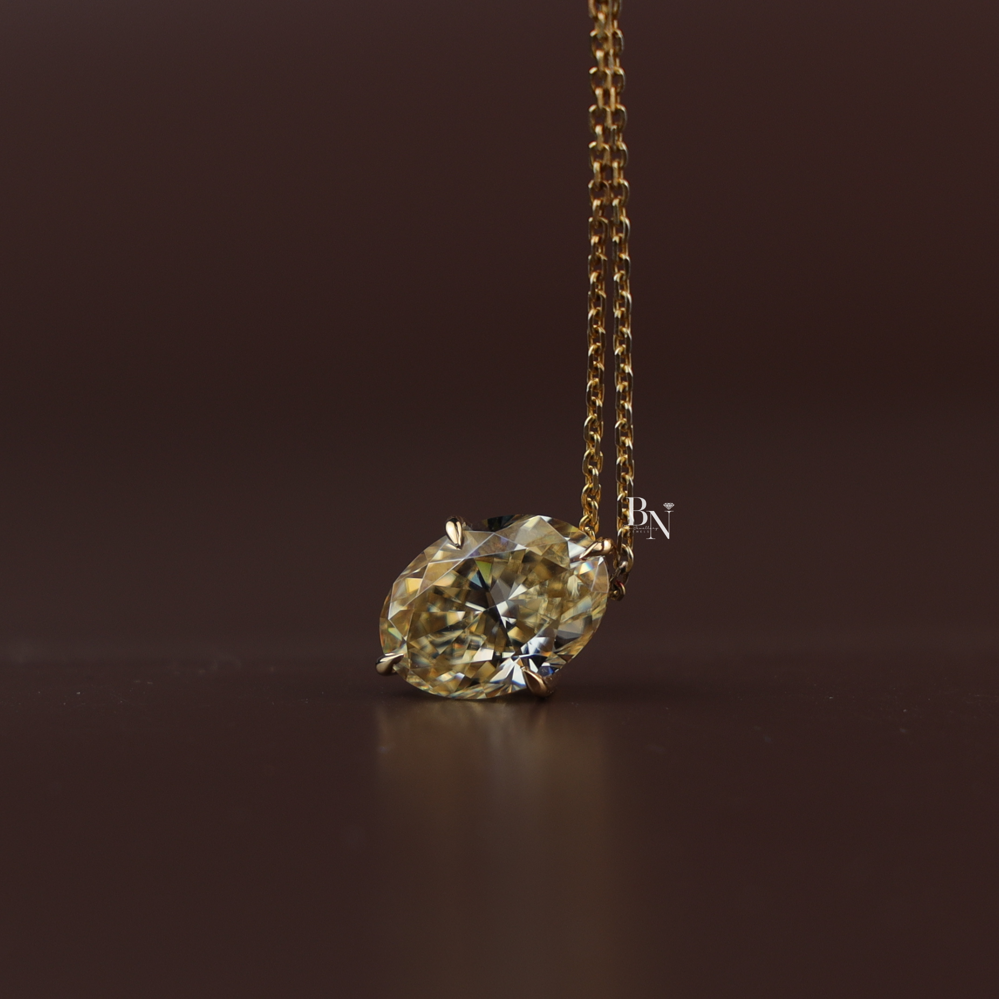 Brilliant cut six carat fancy yellow oval moissanite solitaire pendant necklace displaying exceptional fire set in 14k yellow gold claws on a delicate cable chain shown close up on a model.