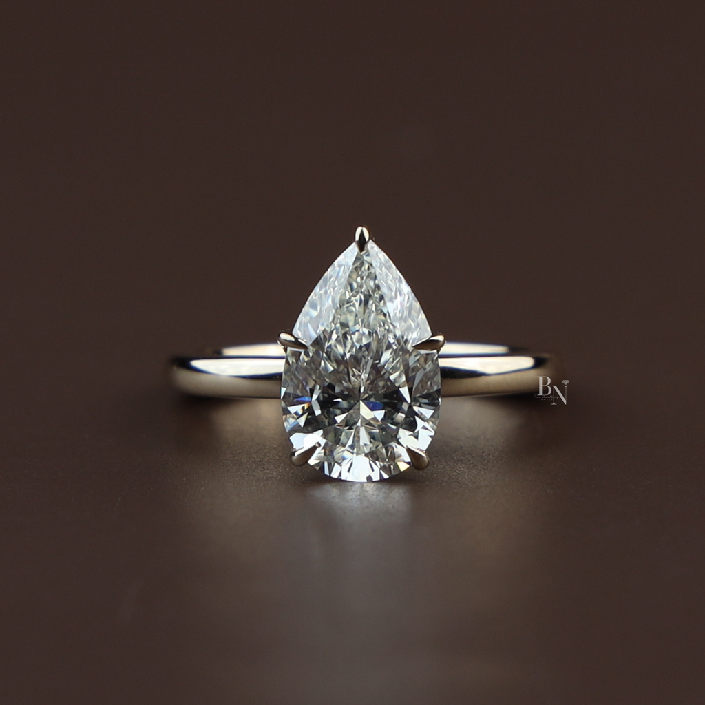 2 carat pear cut lab grown diamond set in a 14k yellow gold lotus petal setting on a whisper thin dainty band showing high brilliance and icy white light return.