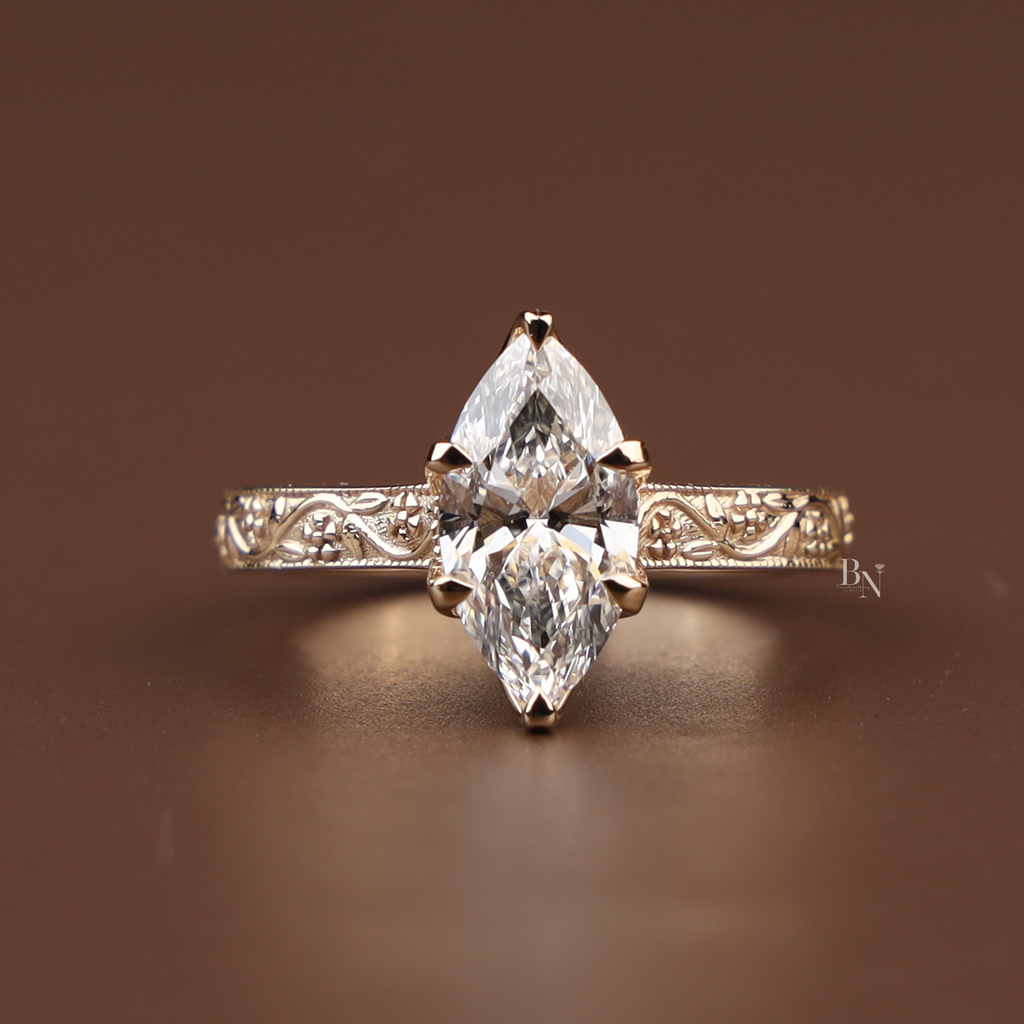 Detailed view of a 2 carat marquise lab grown diamond engagement ring with a vintage hand-engraved scroll band in 14k gold. Luxury bridal.