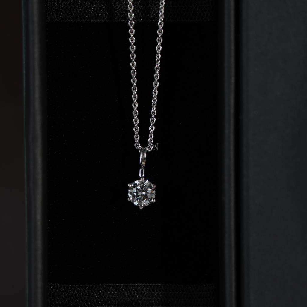 Macro view of a round brilliant cut lab grown diamond solitaire pendant in a 6-prong 14k white gold setting, hanging from a dainty cable chain, showcasing high clarity and crisp white light brilliance.