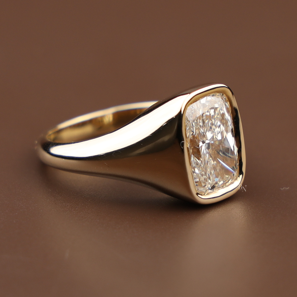 3 carat cushion cut lab grown diamond in a modern 14k yellow gold bezel signet setting on a hand, showing the high-polish tapered band and secure metal frame.