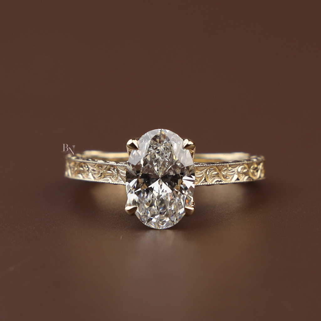 Macro side view of a 2 carat oval cut lab grown diamond engagement ring in 14k yellow gold featuring a hidden halo setting and a detailed hand-engraved vintage filigree band with milgrain edges.