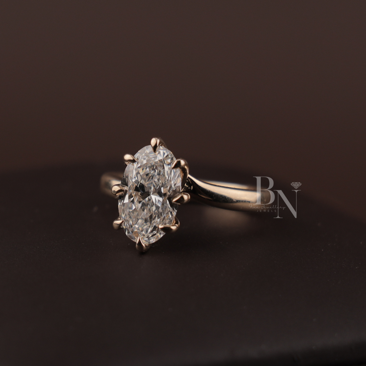 May include: A gold engagement ring featuring a large, clear gemstone. The ring is displayed on a wooden surface, highlighting its design. The band is polished gold, and the gemstone is secured by prongs. A classic piece of jewellery.