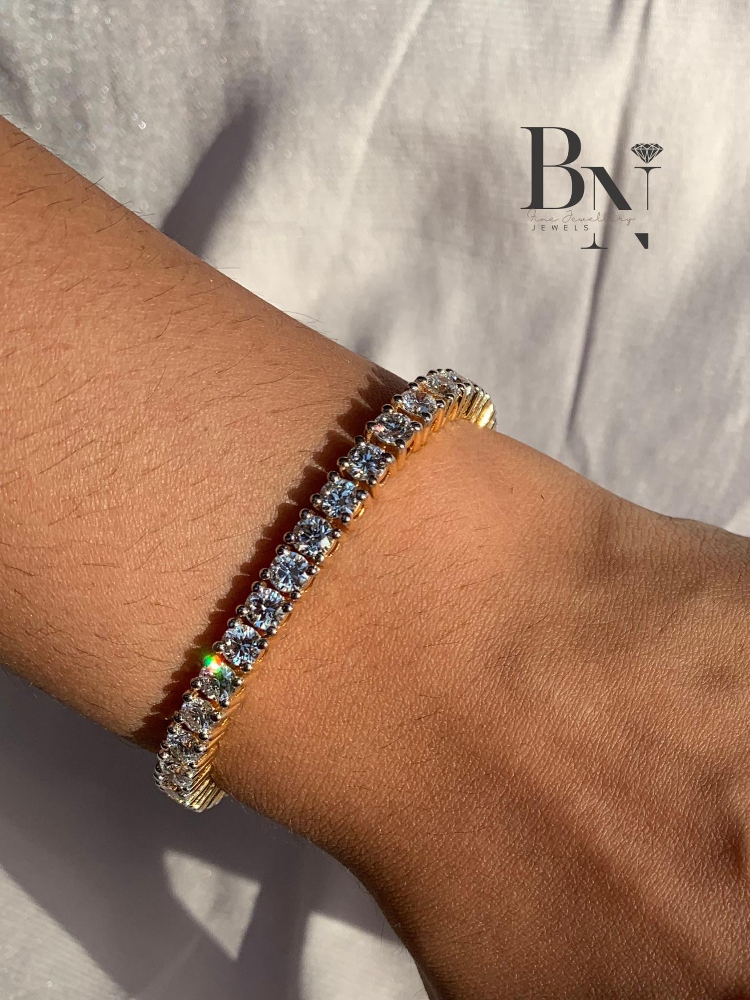 "Model's wrist elegantly wearing a classic 14k gold diamond tennis bracelet. The bracelet features a continuous line of sparkling round diamonds in 4-prong settings, shown in bright, natural light.