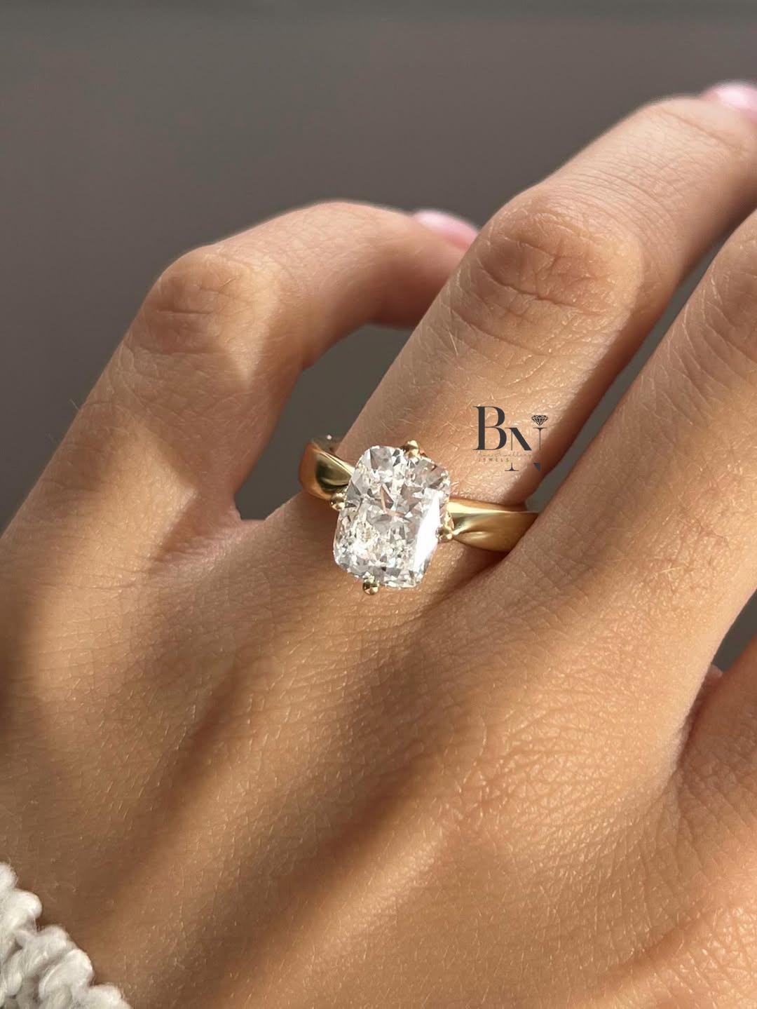 A 3 carat elongated cushion cut lab diamond solitaire engagement ring in 14k yellow gold, worn on a hand to show its impressive size.