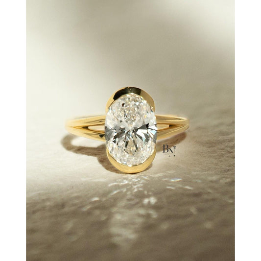 Modern 3.00 carat oval cut lab grown diamond engagement ring with a yellow gold half bezel setting and a delicate split shank band.