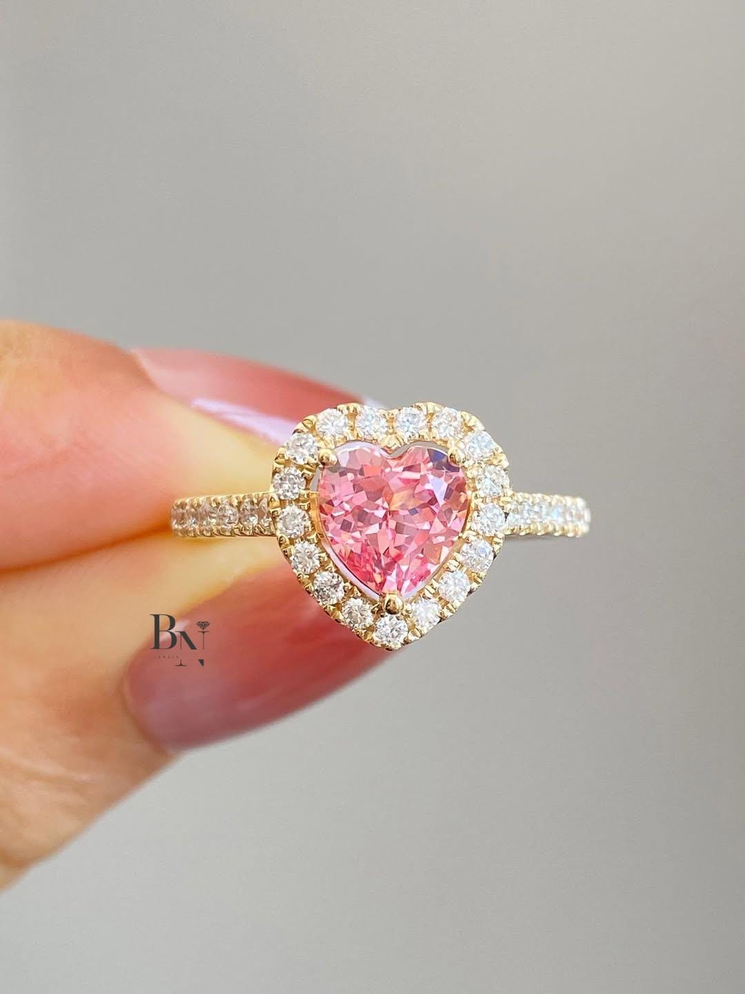 1.50 carat heart shaped pink lab grown diamond ring with a diamond halo and a pavé diamond band in yellow gold.