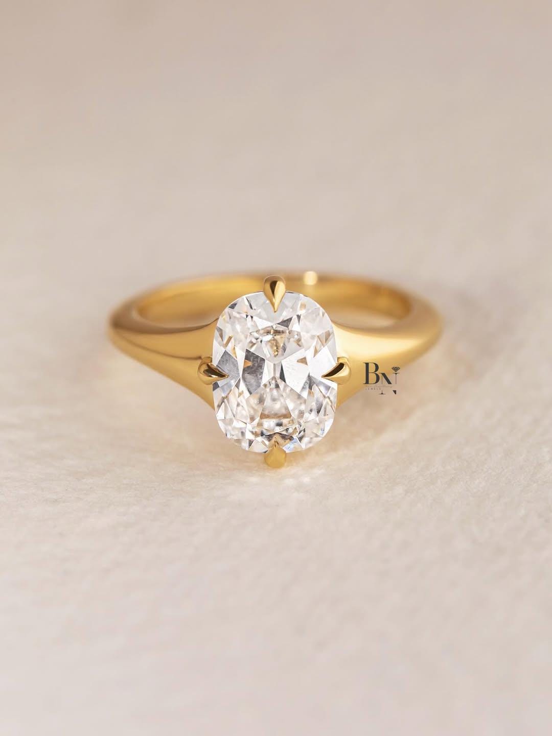 An incredible 2 carat elongated Old Mine cushion cut lab-grown diamond ring held in a box. This ethical statement ring is crafted in a modern, minimalist 14K yellow gold solitaire setting with four compass-style prongs.