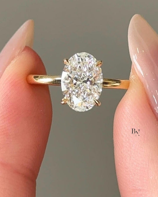 A breathtaking 1.5 carat oval cut lab-grown diamond engagement ring on a finger. This ethical solitaire is crafted in 18K yellow gold and features a modern hidden halo on its basket setting for extra brilliance.