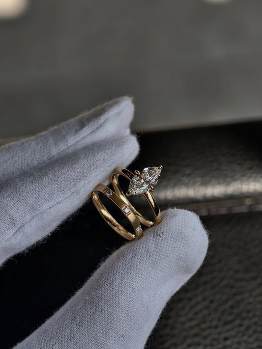 A modern 2 carat marquise lab diamond bridal set in yellow gold, held by gloved hands. The set includes a polished marquise solitaire and a unique matte-finish wedding band with spaced, flush-set IGI certified diamonds.