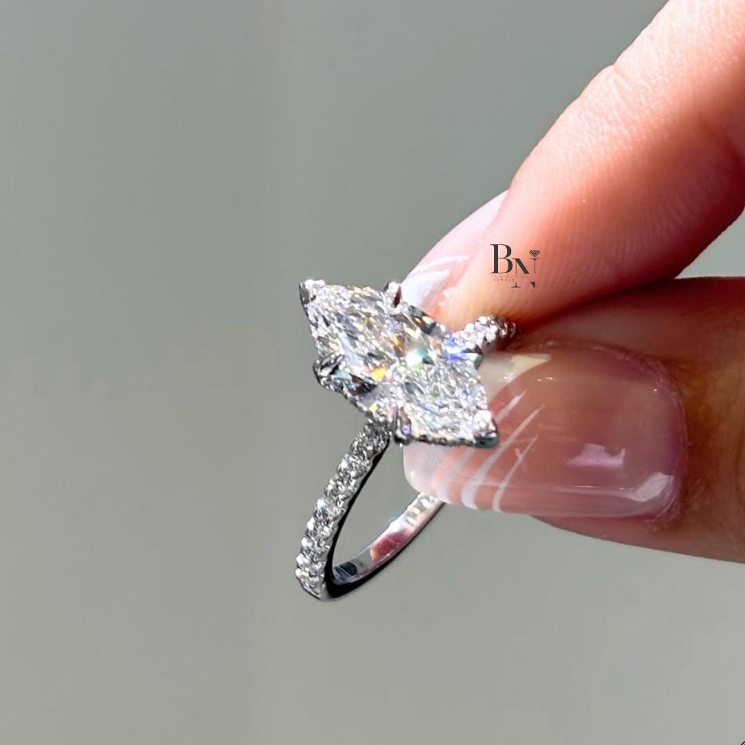 A person holding a 2 carat marquise lab-grown diamond ring between their fingers. The brilliant IGI certified stone is set with a hidden halo on a pave diamond band in white gold, showcasing incredible sparkle from every angle.