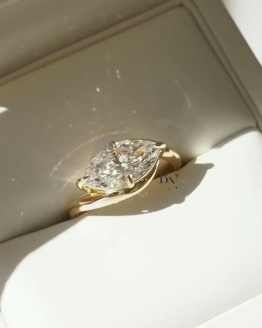 A woman's hand wearing a modern 2 carat East-West marquise lab diamond ring. The artistic bypass design in polished yellow gold wraps around the brilliant IGI certified diamond, creating a unique and minimalist statement.