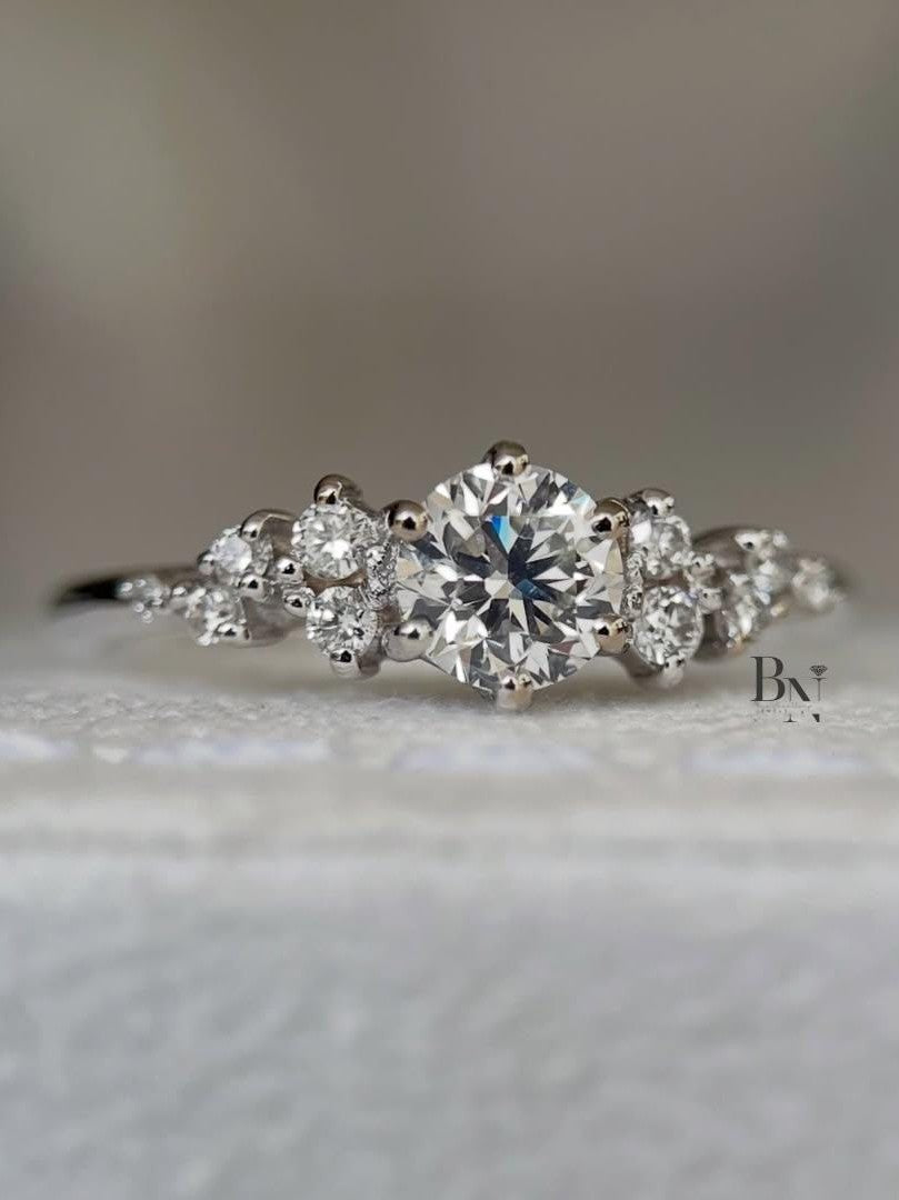 A woman's hand wearing a delicate 0.50 carat round lab diamond cluster ring. The asymmetrical design with multiple small IGI certified diamonds sparkles on a thin white gold band, showcasing its unique, whimsical style.