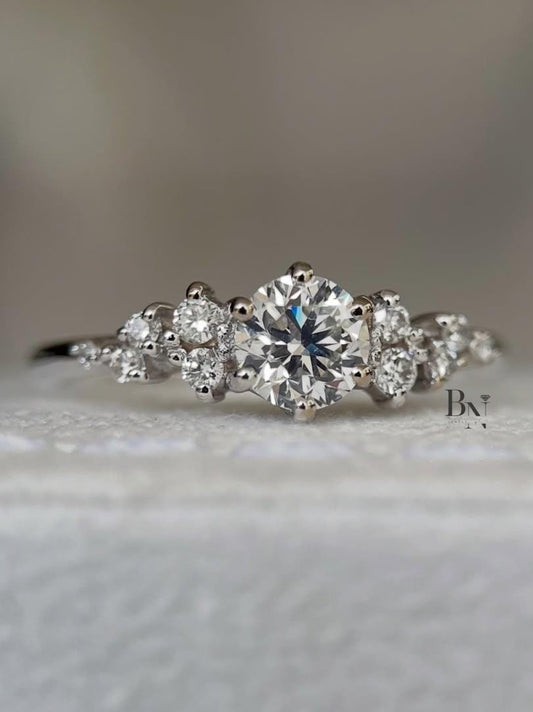 A woman's hand wearing a delicate 0.50 carat round lab diamond cluster ring. The asymmetrical design with multiple small IGI certified diamonds sparkles on a thin white gold band, showcasing its unique, whimsical style.