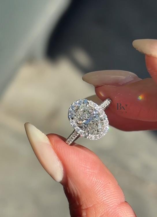 Luxurious 2 carat oval lab grown diamond engagement ring featuring a radiant halo setting and diamond pavé band in polished white gold finish.