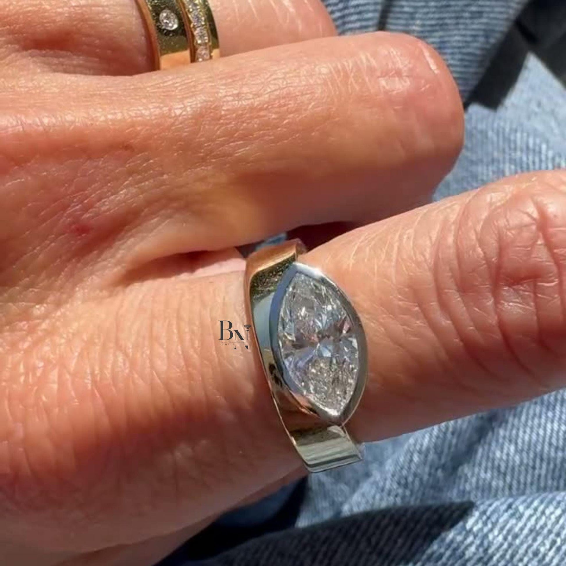 Luxurious 2 carat east-west marquise lab grown diamond engagement ring featuring a thick, wide cigar band in 14k yellow gold. Modern half-bezel horizontal setting.