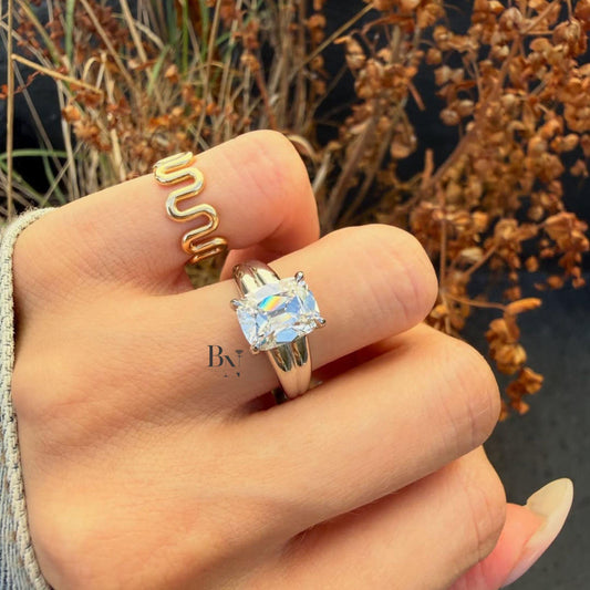 Close up view of a 3 carat Old Mine Cut moissanite solitaire ring featuring secure double claw prongs on a substantial, wide polished band. The vintage-style chunky cushion stone displays brilliant, fiery sparkle. This bold setting represents a modern take on antique style, perfect as a unique engagement ring or luxury statement piece.
