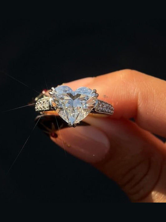 Close-up of a stunning 3 carat Heart Cut Lab Grown Diamond ring with a hidden halo and milgrain accented pave band, set in luxurious two-tone gold and platinum.