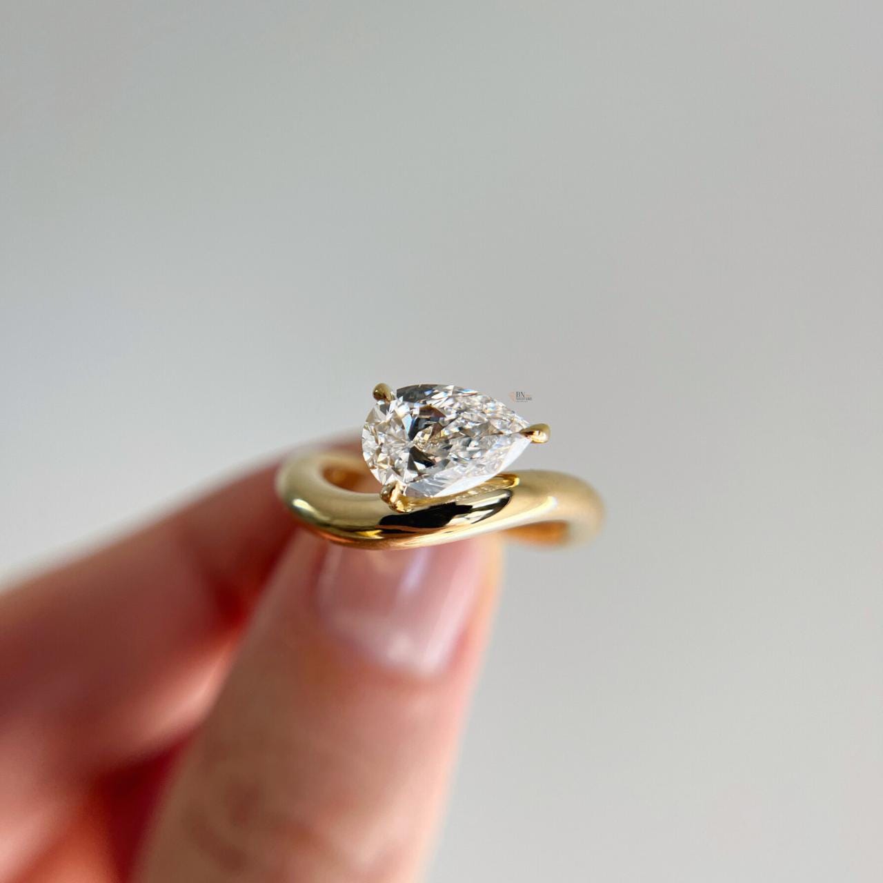 Hand-model view of 1.75 carat Pear Cut Lab Grown Diamond ring with a sleek, chunky swirl bypass setting in high-polished yellow gold, showcasing the modern sculptural design.