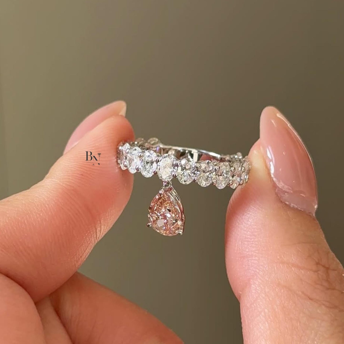 Unique 1.00ct lab grown diamond eternity band in 14k white gold. Features a row of round and oval diamonds and a playful dangling pear cut diamond charm in the center.