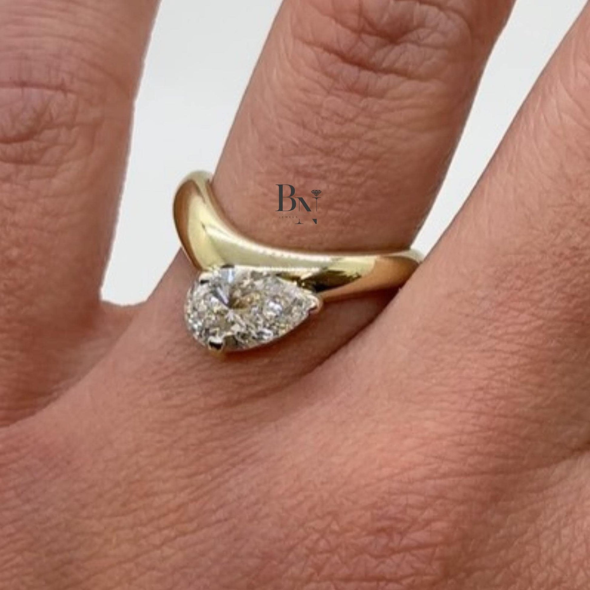 1.00 carat pear cut lab diamond set in a sculptural yellow gold bypass engagement ring, showcasing a bezel setting for a sleek, low-profile look.