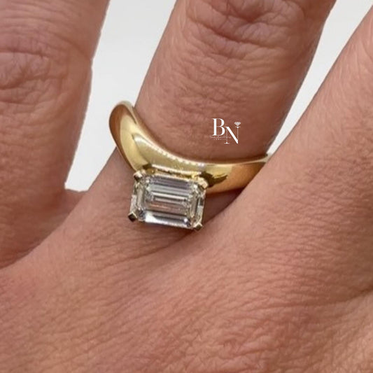 1.00 carat emerald cut lab diamond set east-west in a yellow gold bypass engagement ring, featuring a tension-style setting for a sleek, modern look.