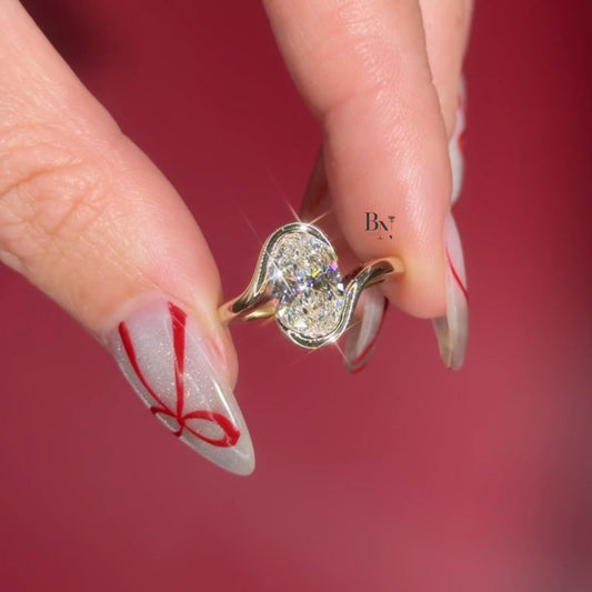 Artistic 3.00ct elongated oval lab grown diamond engagement ring in 14k yellow gold. Features a unique vertical swirl bypass setting with a protective semi bezel on the side.