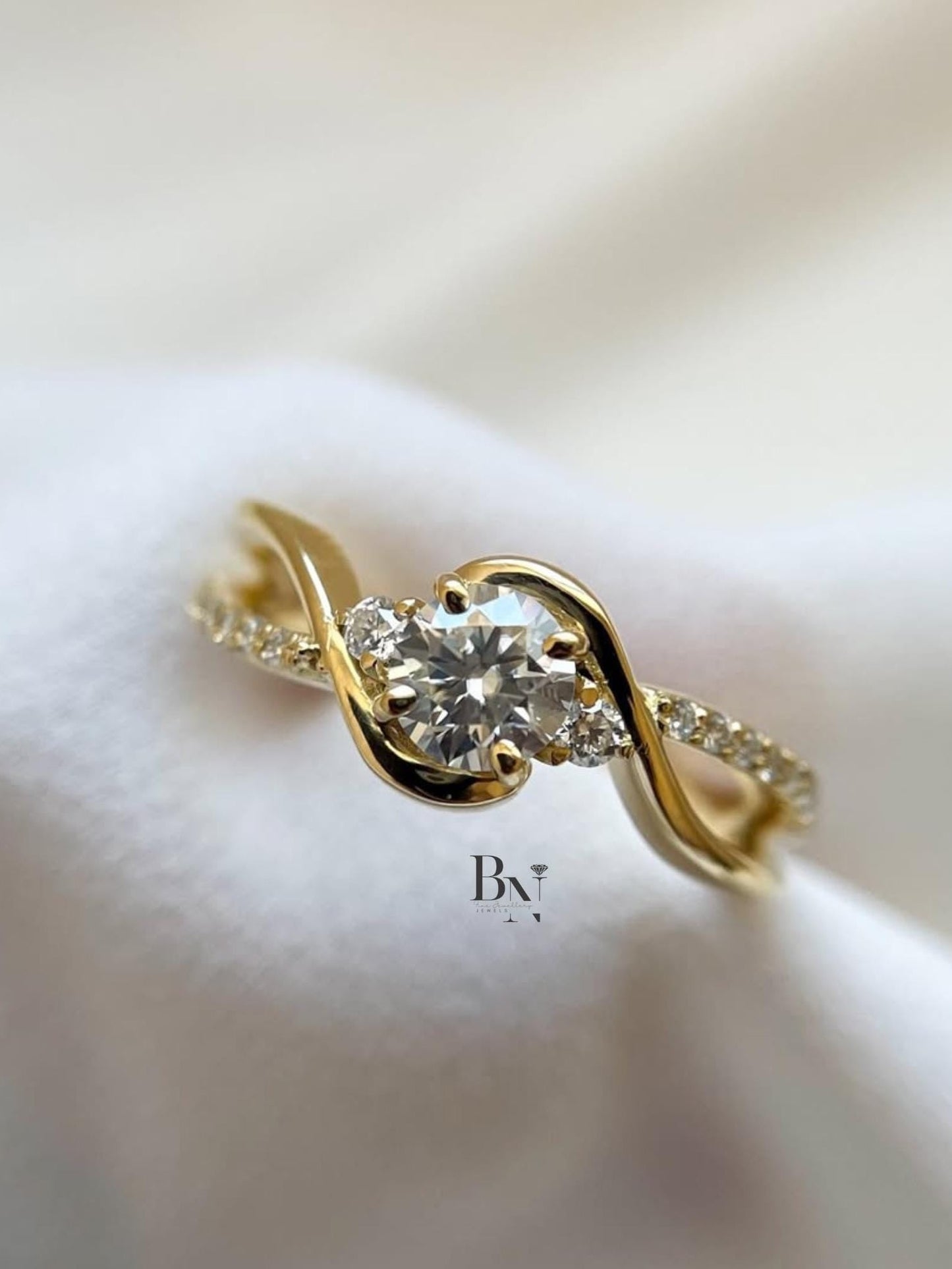 Elegant 1.00ct round brilliant lab grown diamond engagement ring in 14k yellow gold. Features a unique swirl bypass setting with three-stone accents and a micro pave shank.