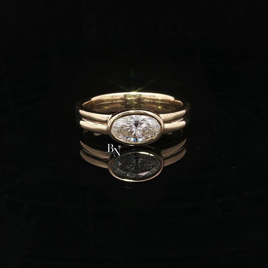 Elegant 1.00ct oval lab grown diamond engagement ring set horizontally (East-West). Secured in a protective full bezel setting with a modern, sculptural double band in 14k yellow gold. A minimalist, quiet luxury statement piece.