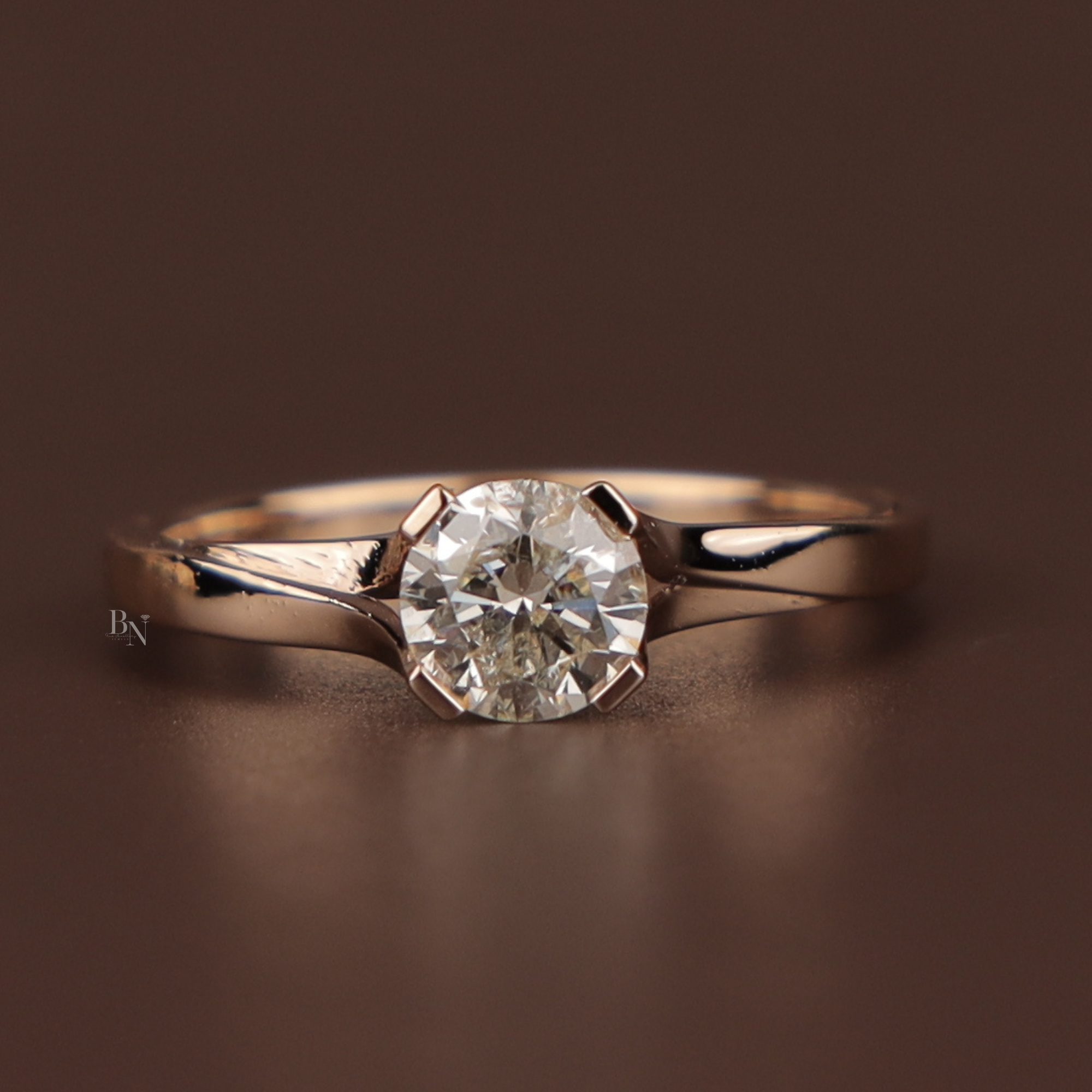 Bypass style engagement ring featuring a round brilliant cut lab grown diamond in a 14k yellow gold tension-inspired setting with a polished overlapping band held between fingers with red metallic nails.
